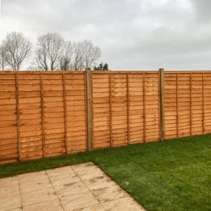 An image showing a line of overlap fence panels installed with a cloudy sky and wooden fence posts