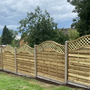 An image showing a cloudy sky which focuses on a row of decorative fence panels recently installed along the grass.