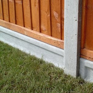 Close up of two fence panels separated by a concrete fence post. The fence panels are fitted on to op concrete gravel boards along grass.